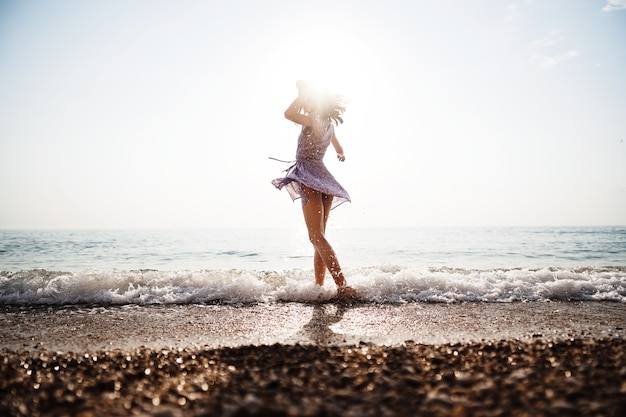 La giovane donna sola cammina sulla riva del mare al tramonto