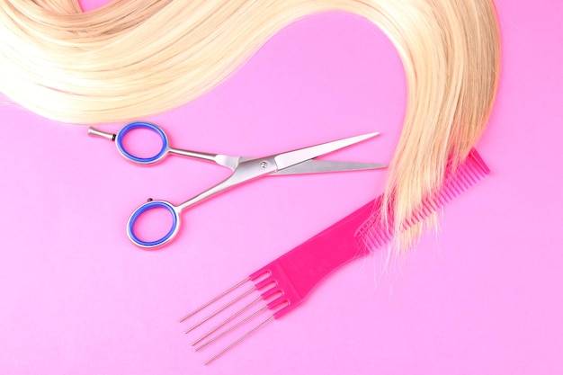 Foto lunghi capelli biondi con pettine e forbici su sfondo rosa