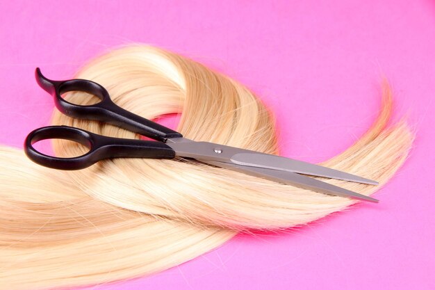 Long blond hair with scissors on pink background