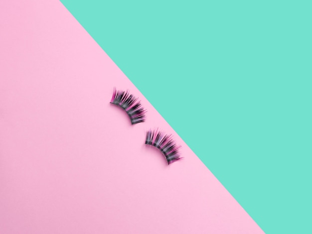 Long colored hairs lashes. Flat lay composition with false eyelashes on pink and turquoise background