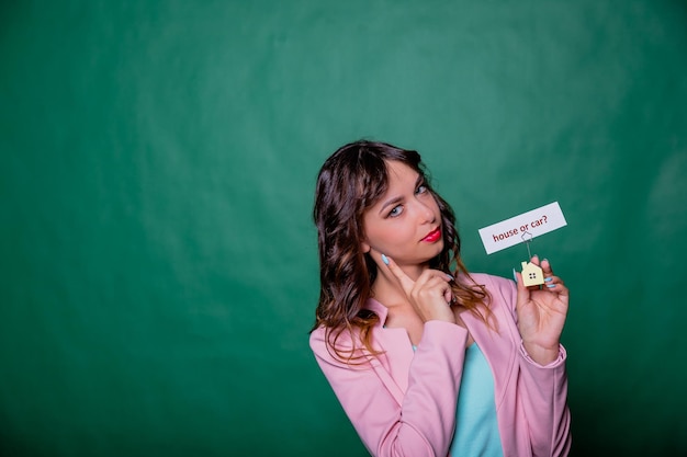 Long curly hair girl facing a choice isolated on green holding small house at her hands with the mes