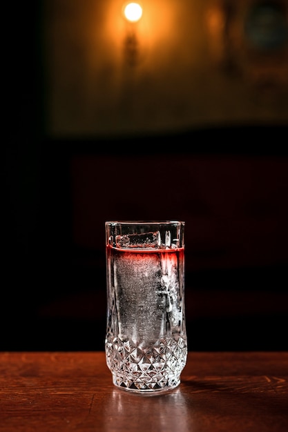 Un long drink trasparente a strati cocktail con ghiaccio in un bicchiere highball in un bar