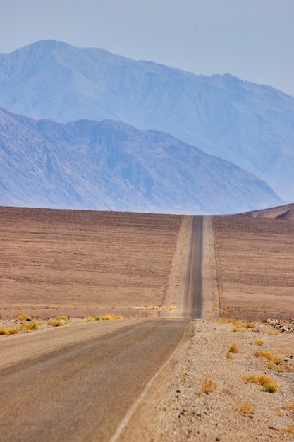 Long and empty desert road in empty plains leading to large mountains