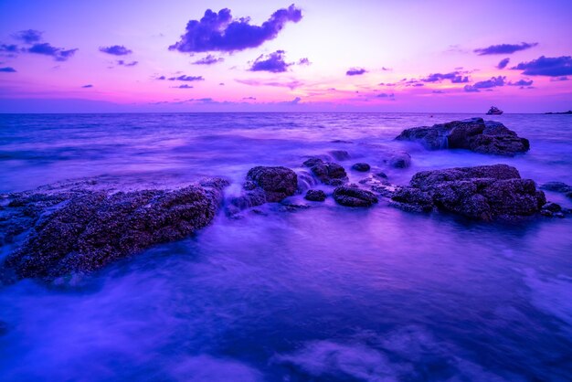 夕日の風景の背景に岩と劇的な空の海の長時間露光画像驚くべき光の自然の風景。