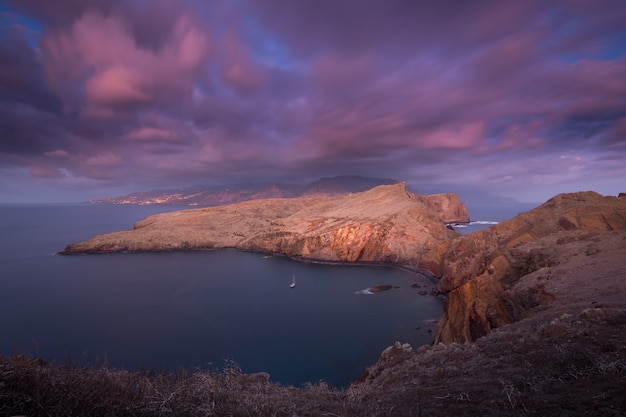 Long exposure landscape at sunrise of a rocky cliff pink blurred fastmoving clouds and lights of a big city in the background