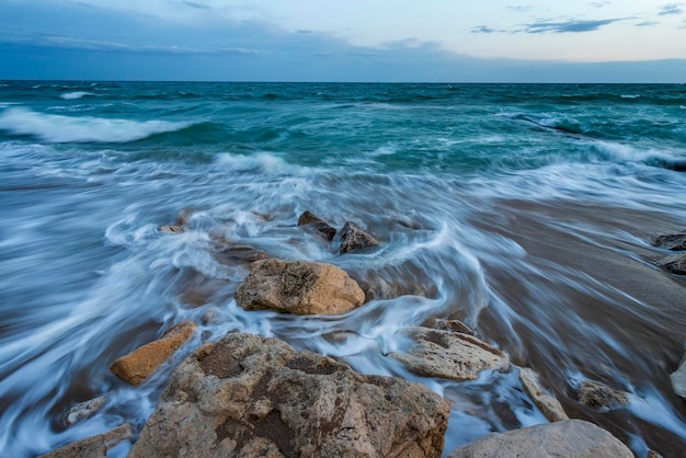 夕暮れ時に岩の間を波が流れる長時間露光の海の風景