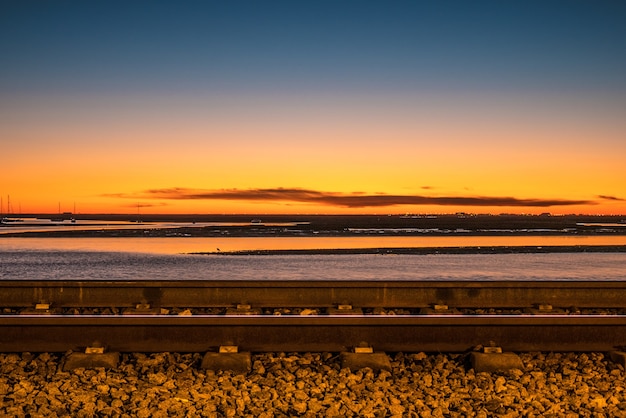 Colpo a lunga esposizione della ferrovia di faro sul tramonto e sul mare.