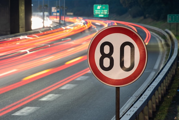 Photo long exposure shot of traffic sign showing 80 kmh speed limit on a highway full of cars in motion blur during the night