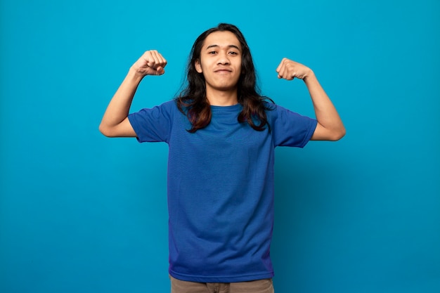 Photo long hair young man raising both clenched fists up demonstrating his strength and masculinity