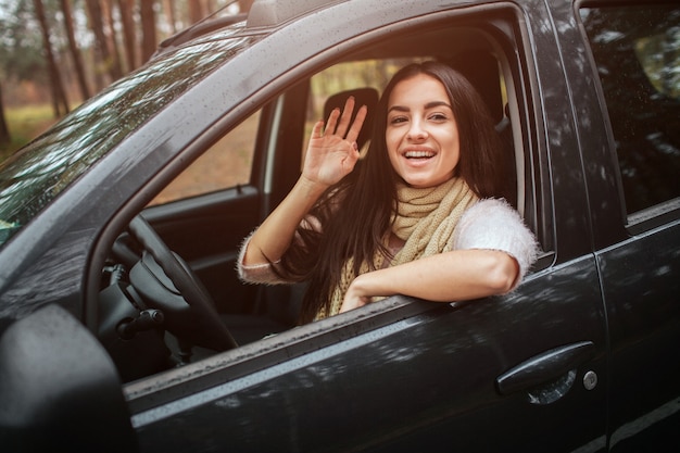 自動車の長い髪のブルネット。女性モデルがセーターとスカーフを着ています。秋のコンセプトです。車で秋の森の旅