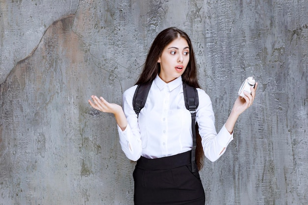 Long haired female student holding alarm clock, shocked about time. High quality photo