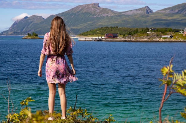 a long-haired girl in a colourful dress walks by the sea on the island of senja in norway