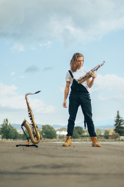 Long-haired saxophonist in black overalls posing with his musical instruments