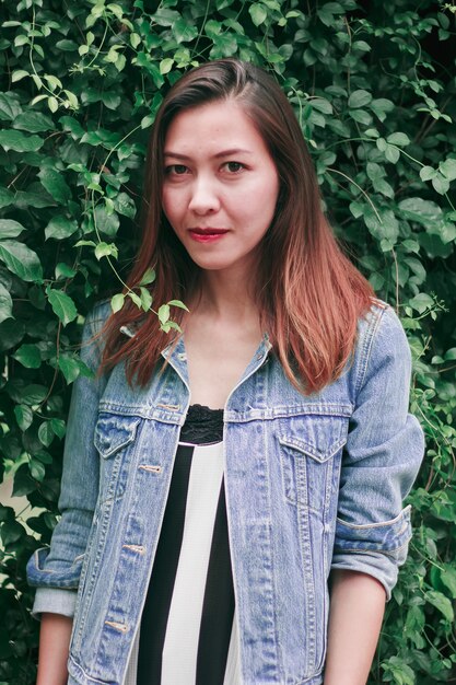 A long haired woman standing against a tree wall