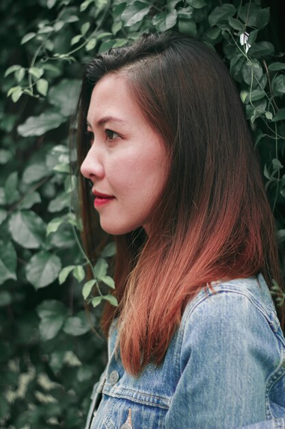 A long haired woman standing against a tree wall