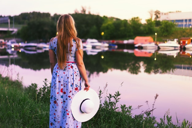 A long haired womanwith a white hat and a beautiful long dress