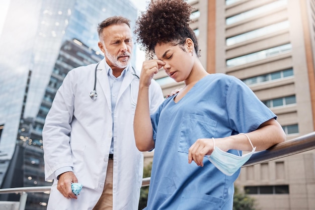 Long hours can take a toll when youve worked nonstop Shot of a young female nurse suffering from a headache while talking to a colleague in the city