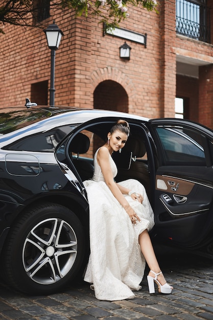 Long legged brunette model girl with bright makeup in a trendy silver dress sits in the luxury car