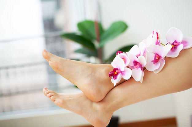 Photo long legs of a woman with a fresh manicure and orchid flowers.