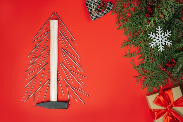 長い釘とハンマー、トウヒの枝と赤い背景のギフトボックス、フラットレイとクリスマスツリーの形にレイアウト