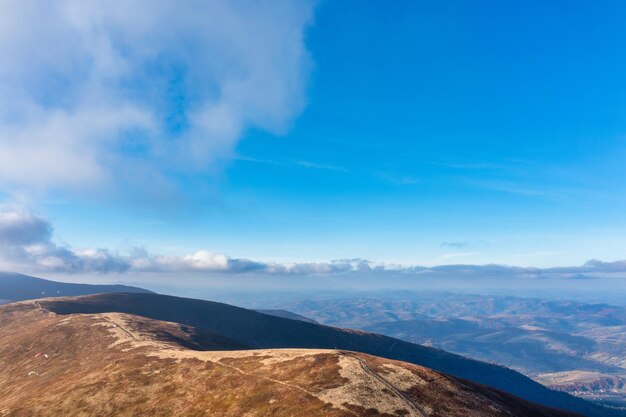 Long narrow pathways running along high mountain ridge under white fluffy clouds floating on blue sky on sunny day aerial view