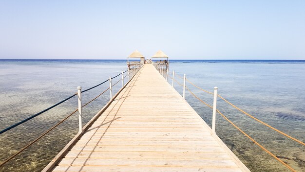 Длинный понтон на берегу Красного моря в Египте. Понтон для спуска в воду. Деревянный мост на территории отеля Amway в Шарм-эль-Шейхе с металлическими ограждениями и канатом через море с волнами.