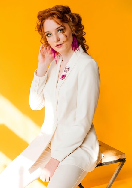 Long purple ostrich feather earrings and beetle brooches on a redhaired girl in a white jacket Girl posing on orange background