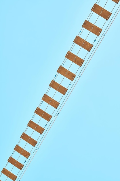 Long rope bridge with wooden planks against blue sky Fun attraction water park at summer resort