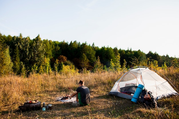 Long shot of man looking at the forest next to his tent