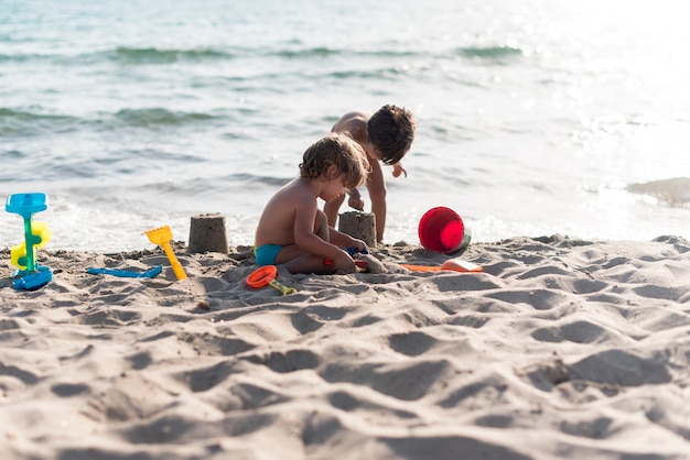 Foto fratelli lunghi sparo che fanno castelli di sabbia sulla spiaggia