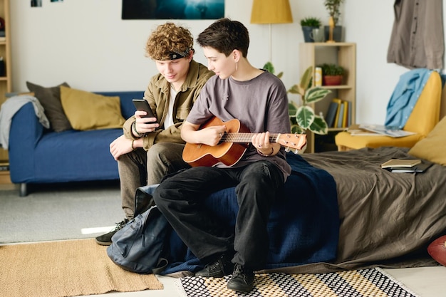 Long shot of two teenagers in casualwear looking at smartphone screen