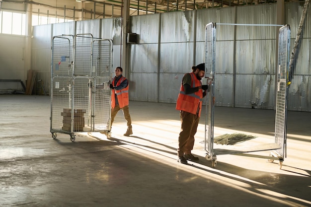 Long shot of two young male engineers in workear pushing and repairing carts