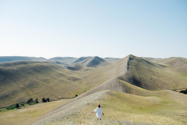 Long shot of a woman in a white dress standing on a hill ridge, surrounded by a beautiful scenery