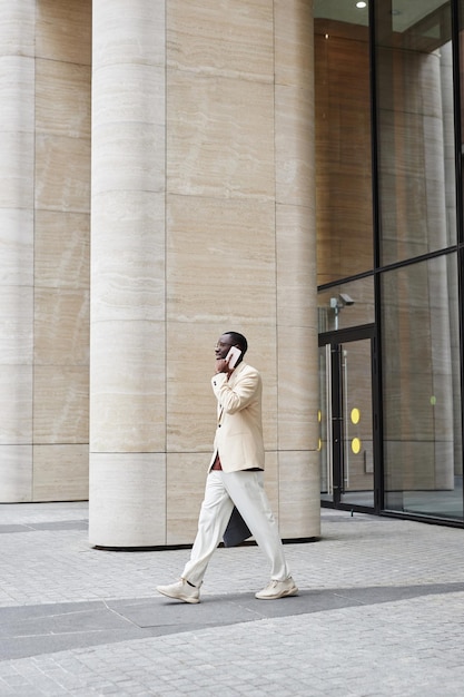 Long shot of young black man in elegant suit moving along buisiness center