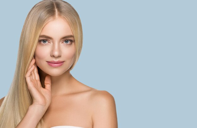 Foto acconciatura bionda del ritratto della donna di bellezza dei capelli lunghi lisci. toccandole il viso. colore di sfondo. blu