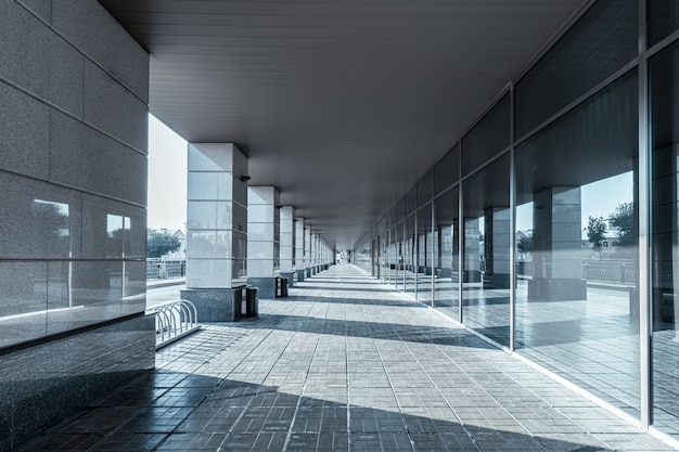 A long straight gallery in a modern building has minimalist columns and mirror glass wall