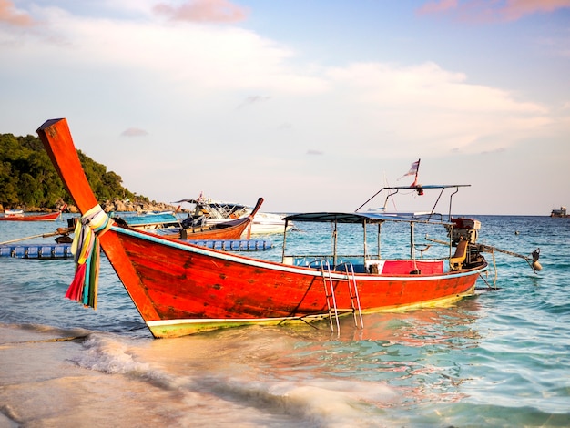 日没の照明、コ・リープ、タイで熱帯の島の白い砂浜に長い尾のボート