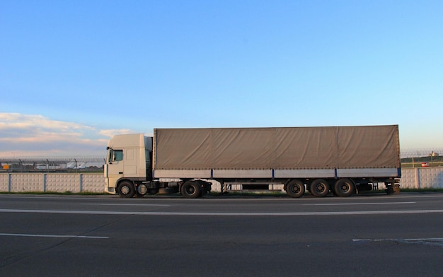 Длинный грузовик на шоссе возле забора транспортного аэропорта с самолетами