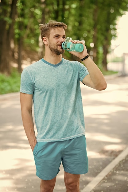 Long workout is over Man with athletic appearance holds bottle with water Athlete drink water after training in park on sunny day Man athlete in sporty clothes drink refreshing mineral water