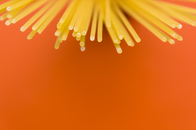 Photo long yellow spaghetti pasta on orange background yellow italian pasta italian food and kitchen concept copy space