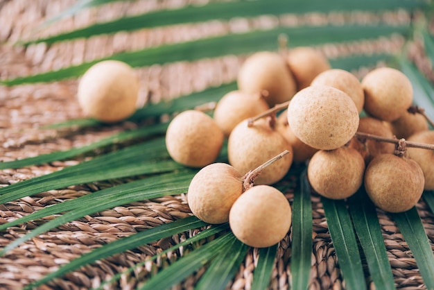 Photo longan fruits over palm leaves on rattan background copy space dimocarpus longan bunch of exotic longans tropical food concept