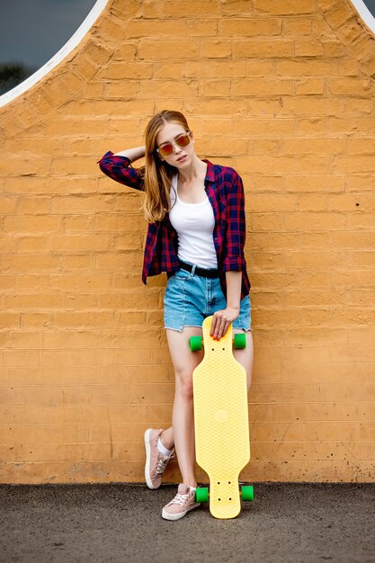 longboarding meisje staat naast de bakstenen muur