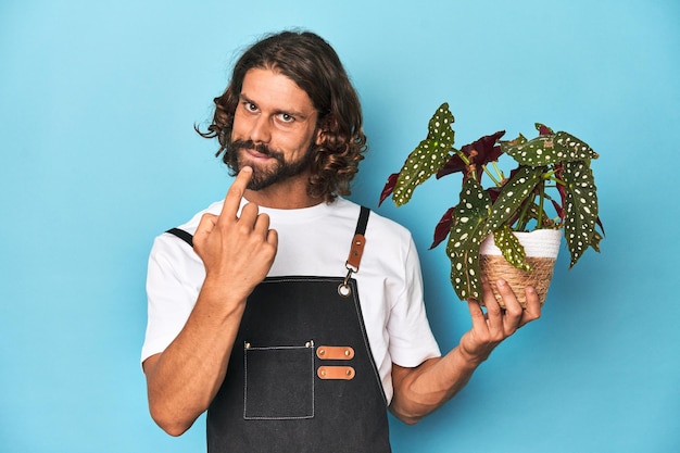 Longhaired gardener with beard holding a plant pointing with finger at you