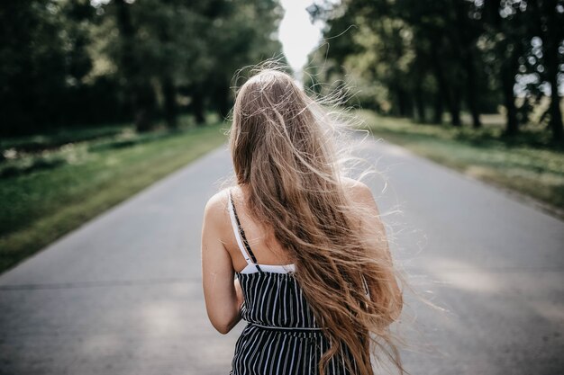 긴 머리 소녀의 뒷모습은 더 밝은 미래를 만나기 위해 두려움에서 도망치는 숲길을 따라 달린다