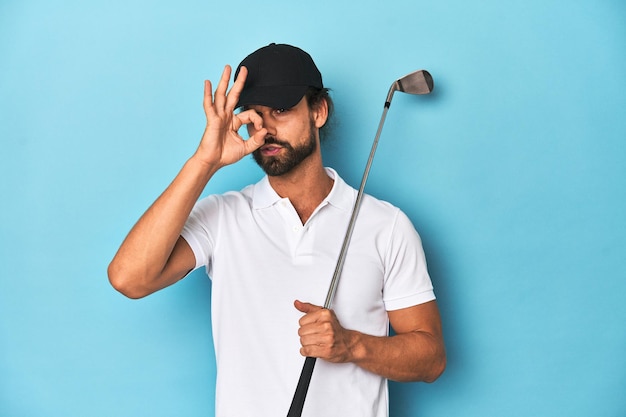 Foto golfista dai capelli lunghi con mazzo e cappello eccitato che tiene il gesto ok agli occhi