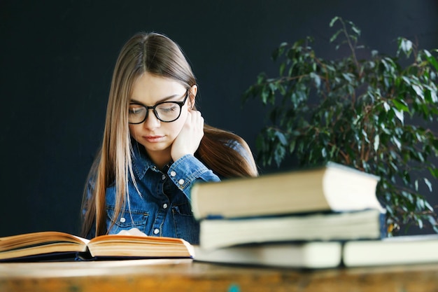 Longhaired student girl wearing glasses sitting by wooden table and preparing to the exams