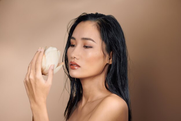 Longhaired woman in top with bare shoulders holding dried lotus buds on beige background