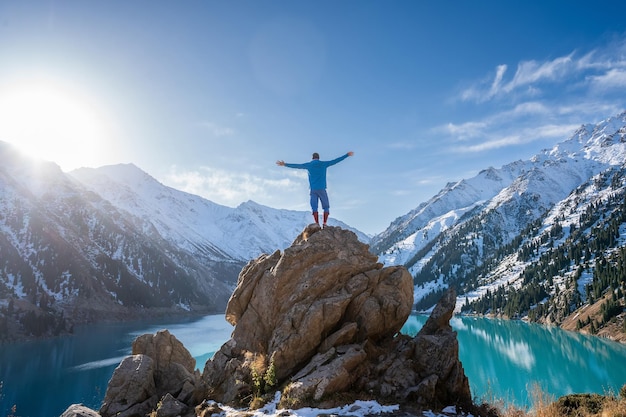 Longshot of a man standing on a boulder on a vantage point over\
a mountain lake