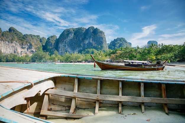 Longtailed boats o tropical beach halfsubmerged old wooden boat mountains and blue cloudy sky