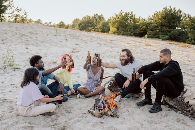 Longtime friends meet at the lake on the beach by the fire sit on the sand on wooden logs